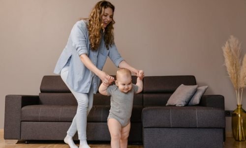 A joyful moment of a mother guiding her baby as they play together indoors.