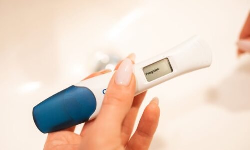 Close-up view of a positive digital pregnancy test held by a woman with manicured nails.